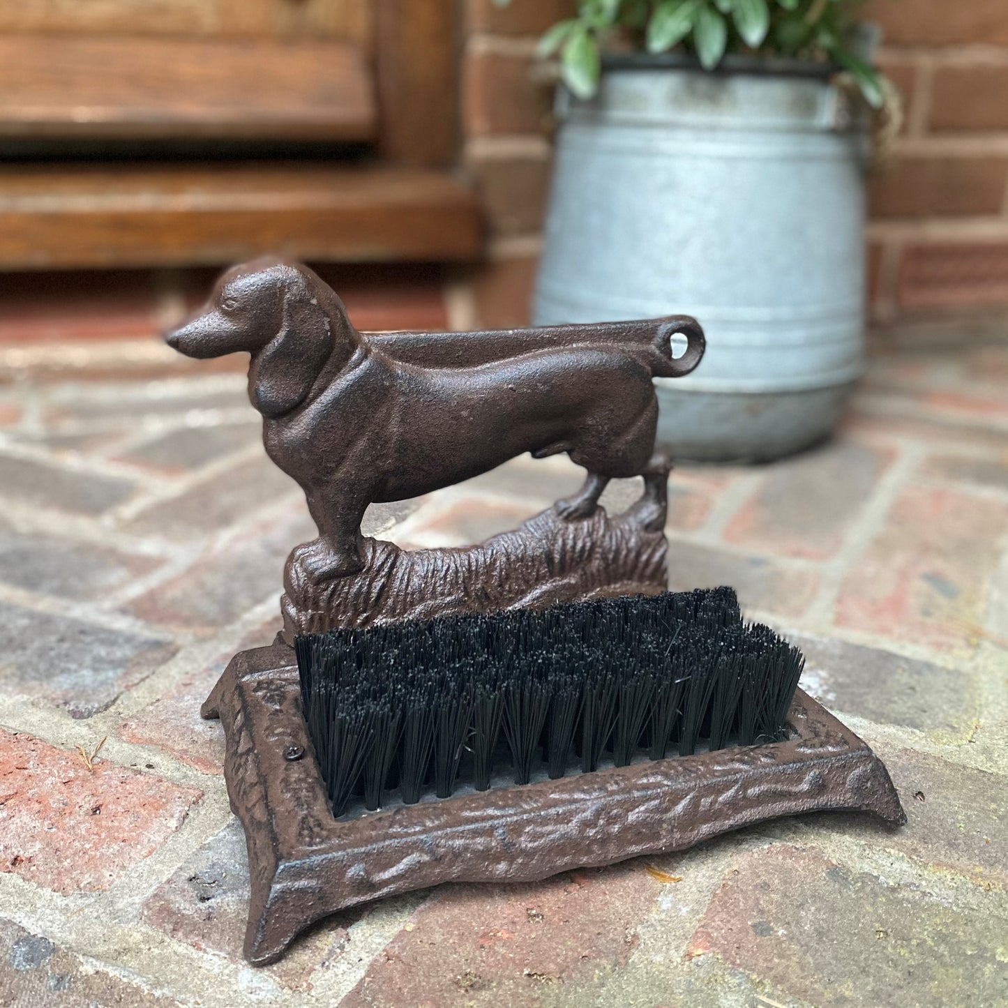 A cast iron shoe scraper with a motif of a dachshund dog. It has bristles on the base for cleaning shoes.