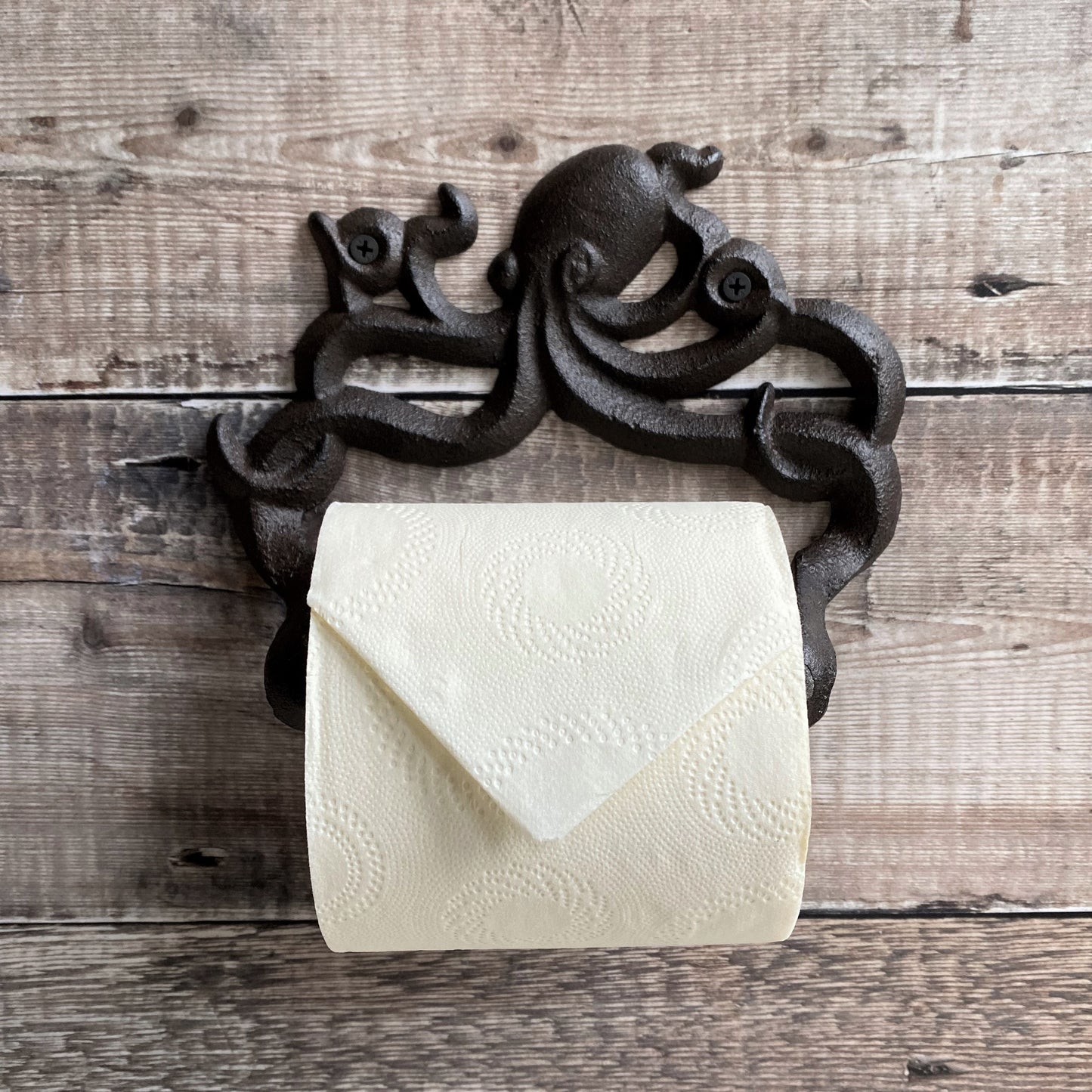 A wall mounted cast iron toilet paper holder with an octopus design, filled with a roll of toilet paper.
