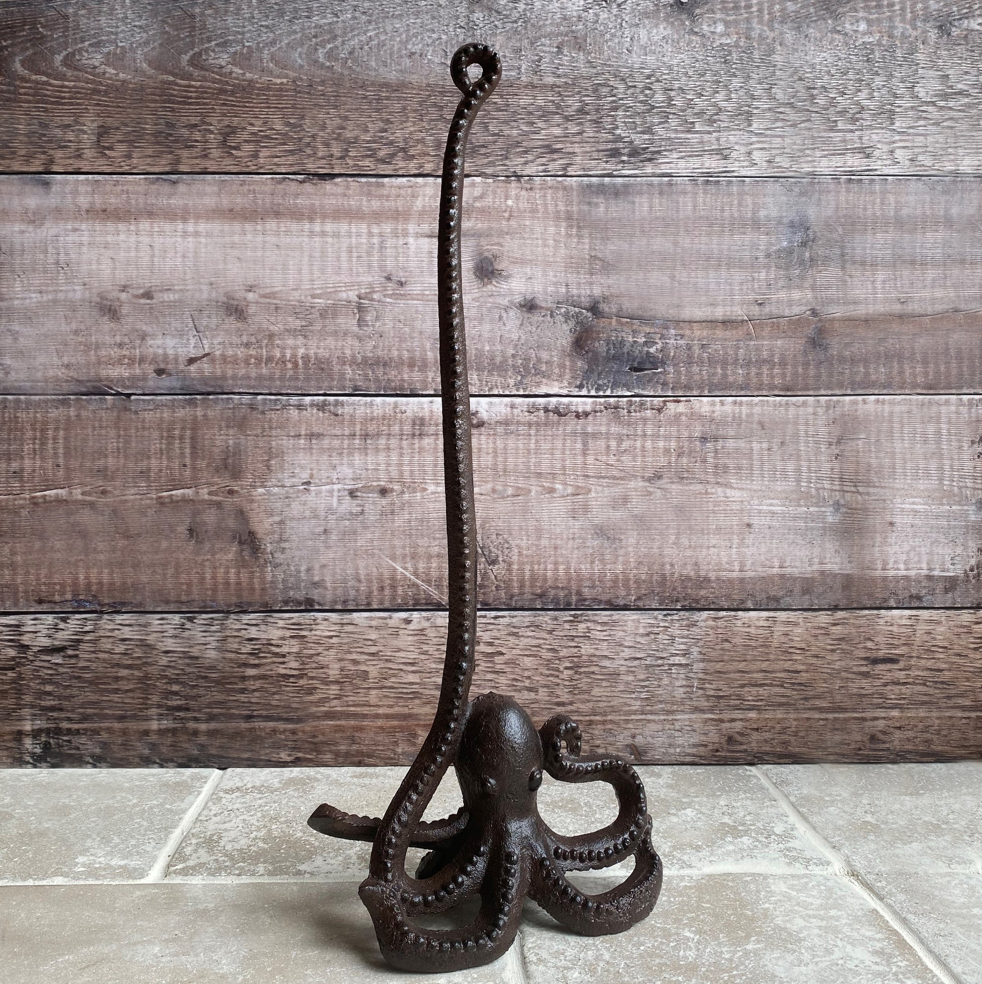 A cast iron loo roll holder in the shape of an octopus with one long tentacle pointing in the air, set against a wooden backdrop.
