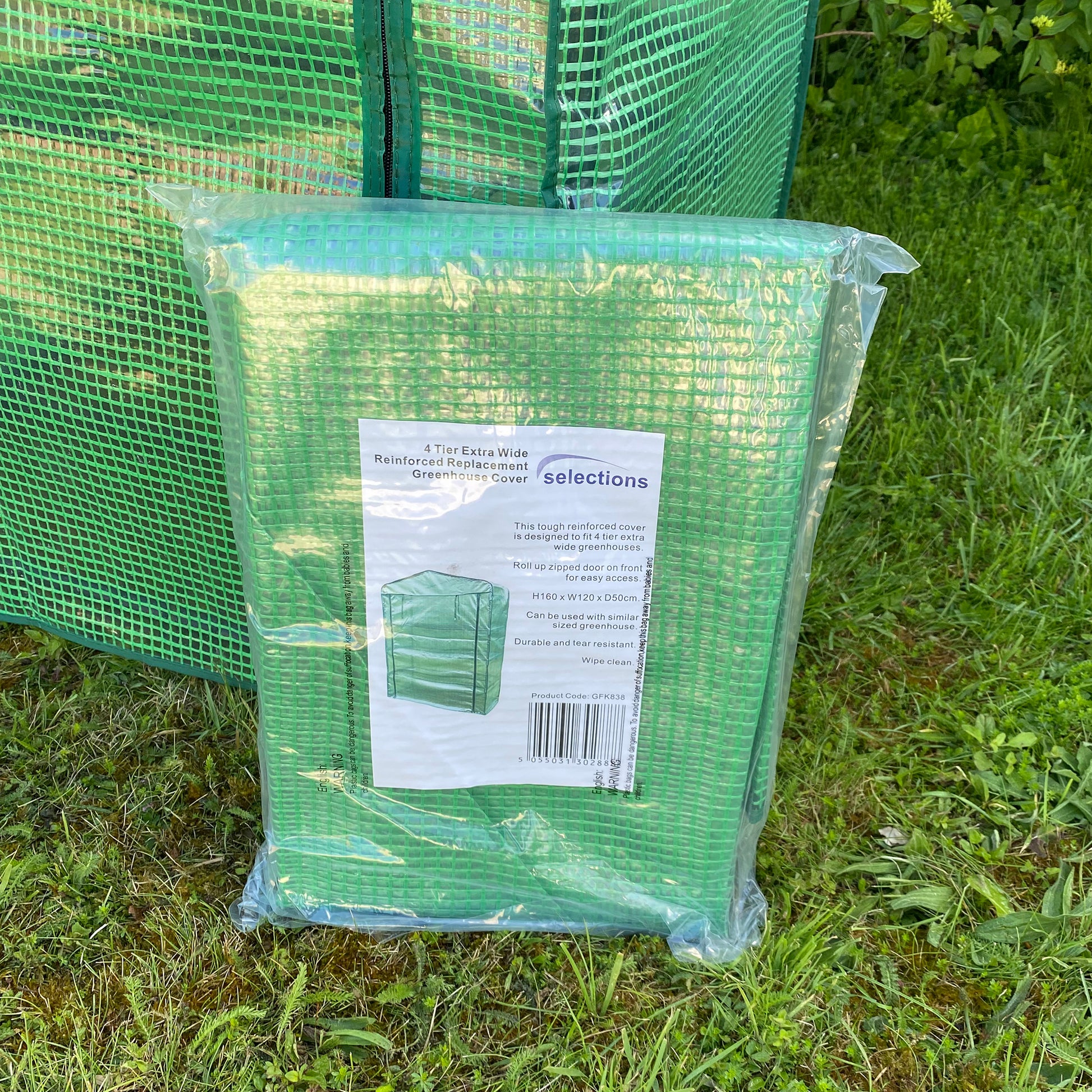 A packaged green replacement cover for a greenhouse, displayed outdoors on grass.