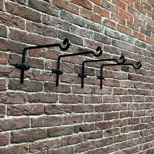 A set of four black metal square hanging basket brackets mounted on a brick wall.