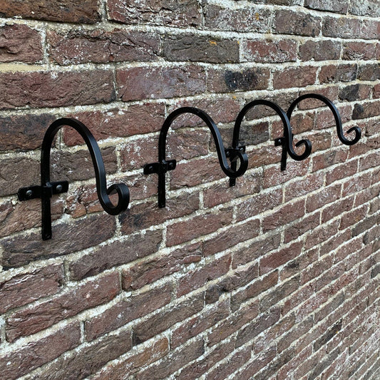 A set of four black metal round hanging basket hooks mounted on a brick wall.