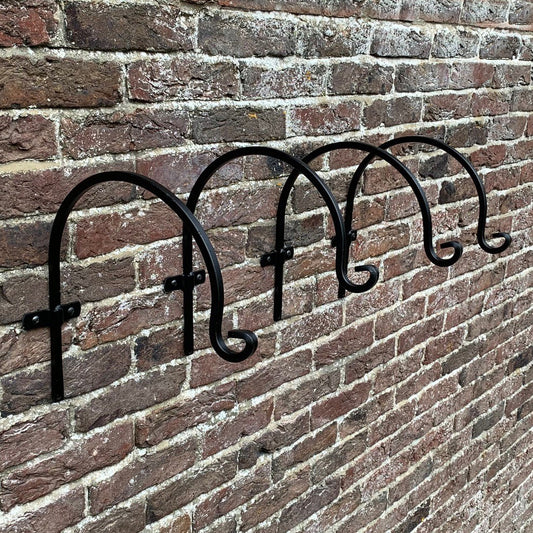 A set of four black metal round hanging basket hooks mounted on a brick wall.
