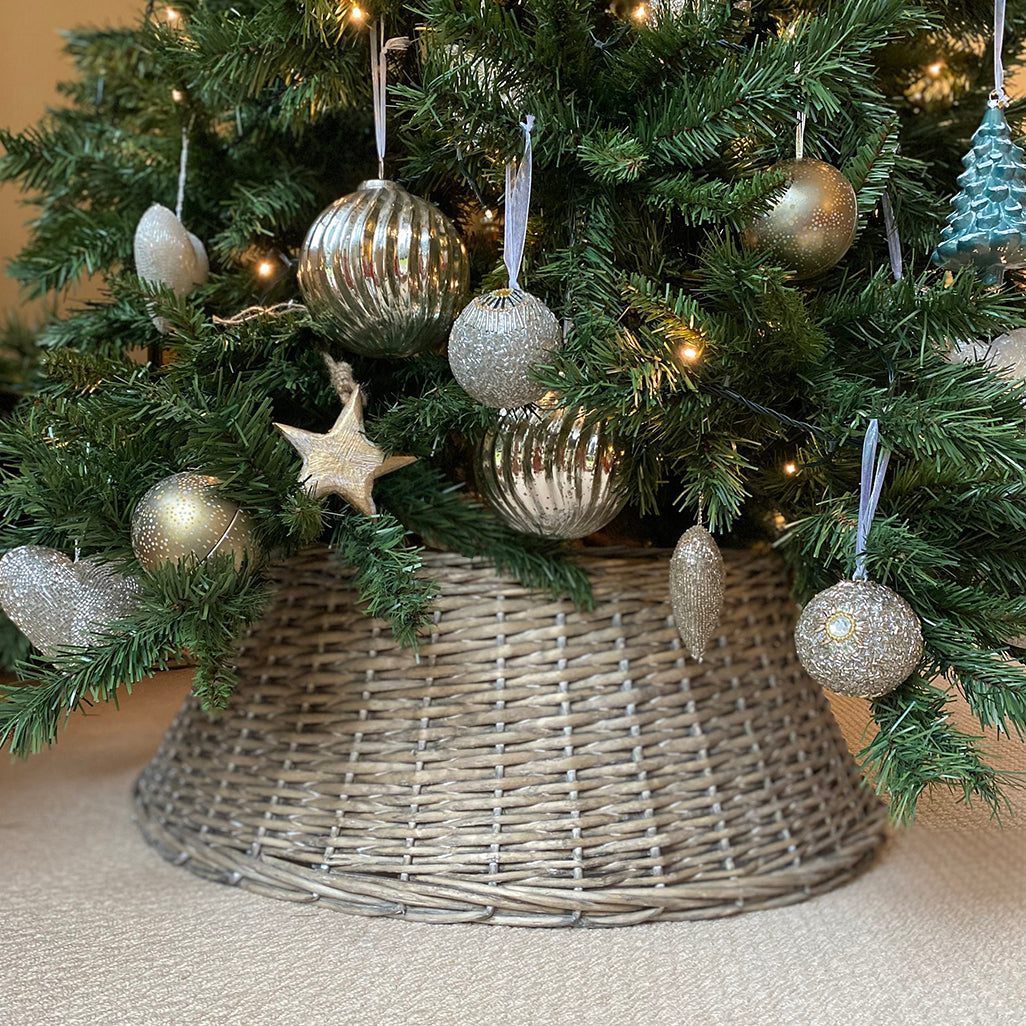A Christmas tree skirt made of grey wicker, placed under a decorated Christmas tree to disguise the base.