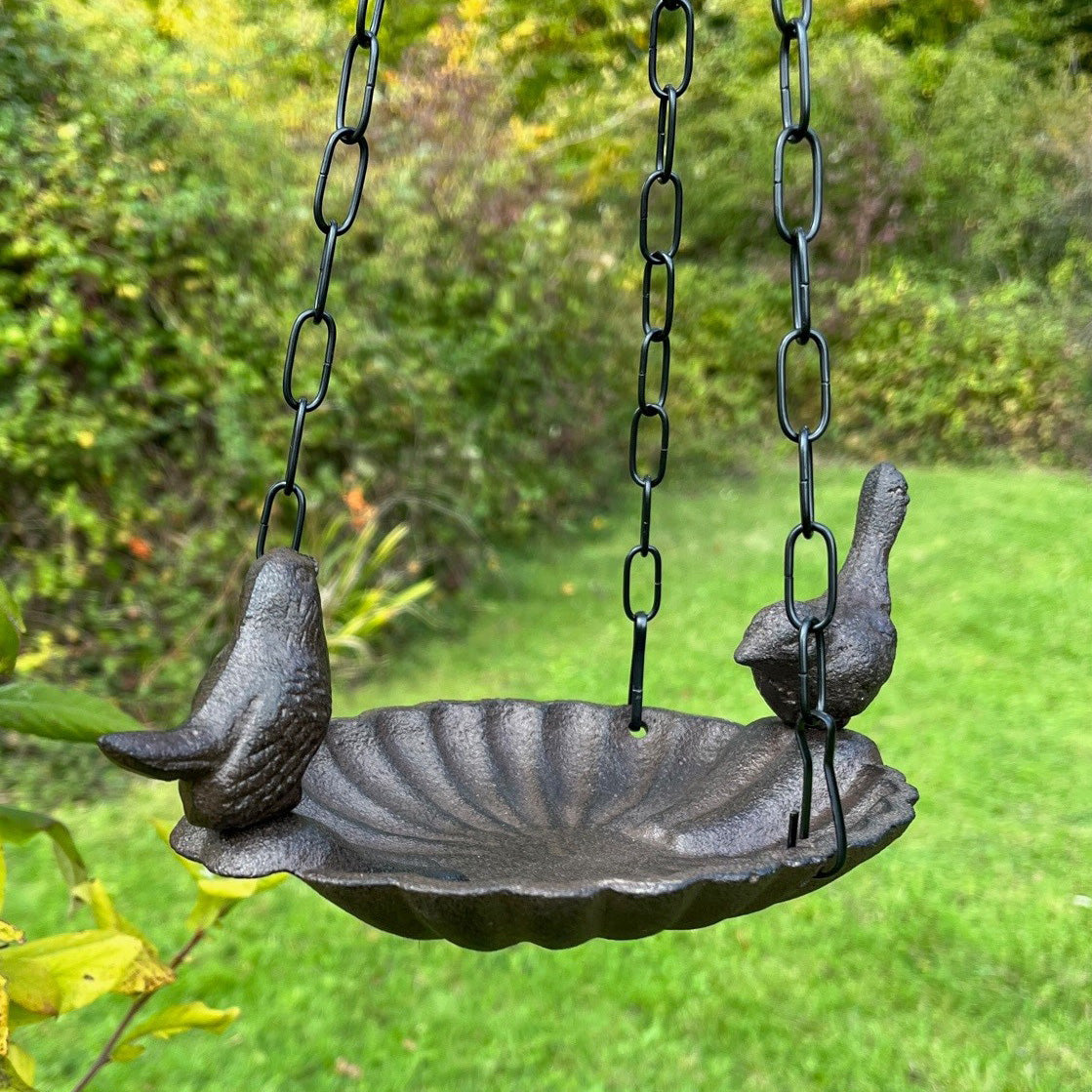 A gray cast iron bird bath hanging from chains, featuring two birds as decorative elements on either end of the dish.