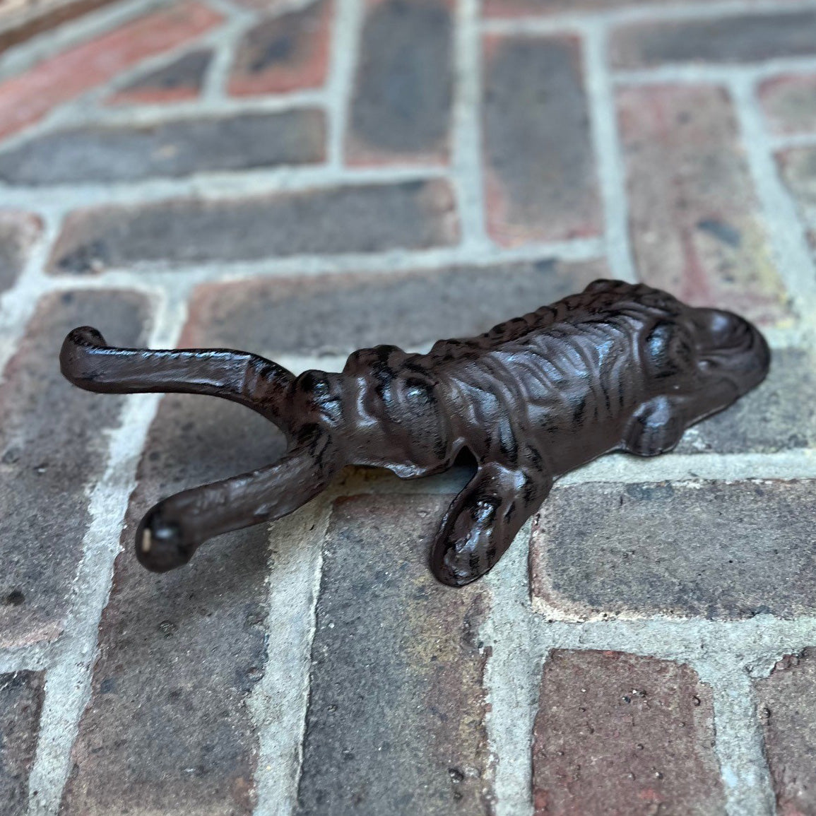 A cast iron boot jack designed in the shape of a dog lying down, placed on a brick surface.