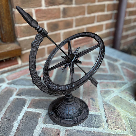 A vintage style cast iron garden sundial with a base resembling the globe, longitude and latitude lines, and landmass outlines. It features roman numerals and a supporting rod.