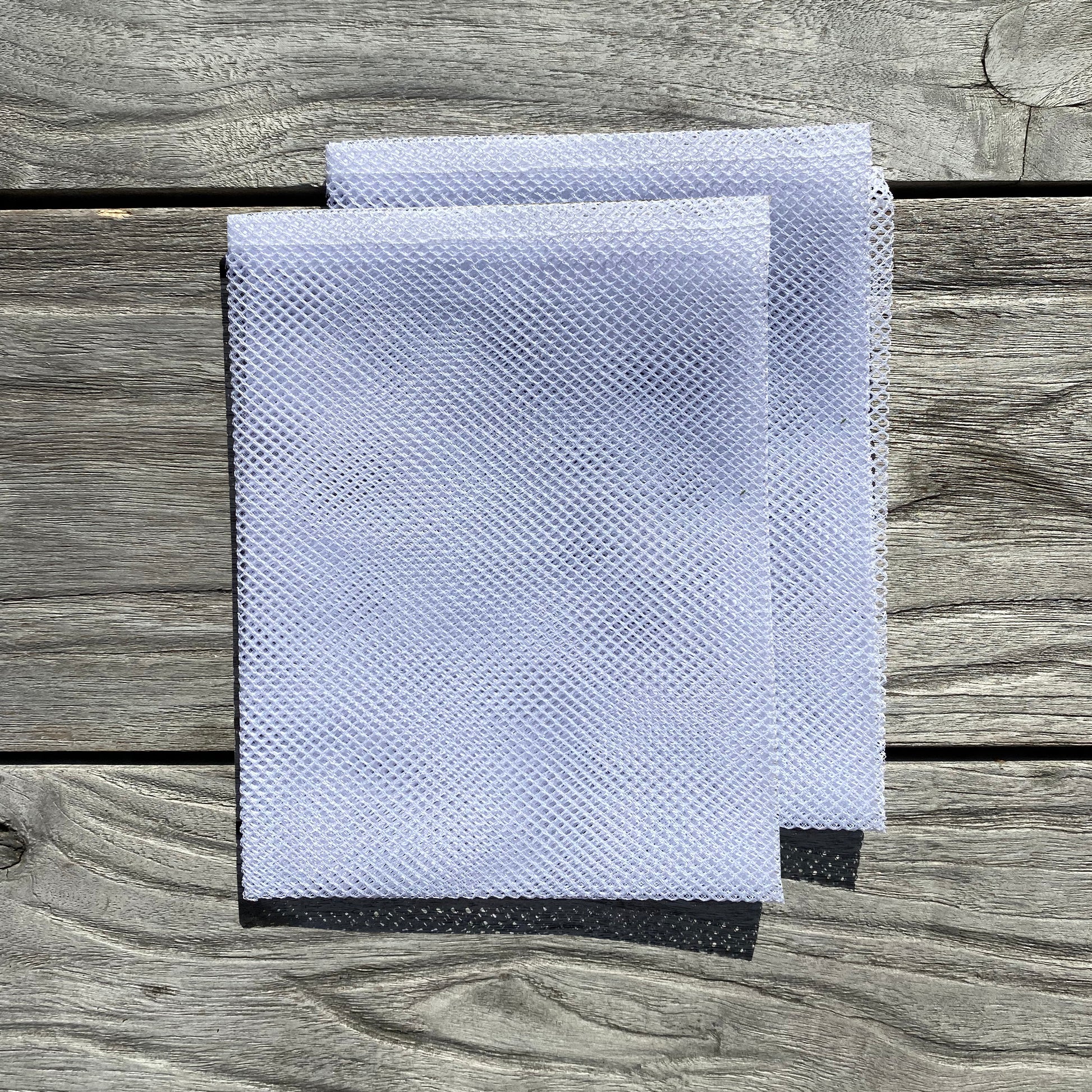 Two white mesh straining bags designed for use with a 6 litre apple press, placed on a wooden surface.