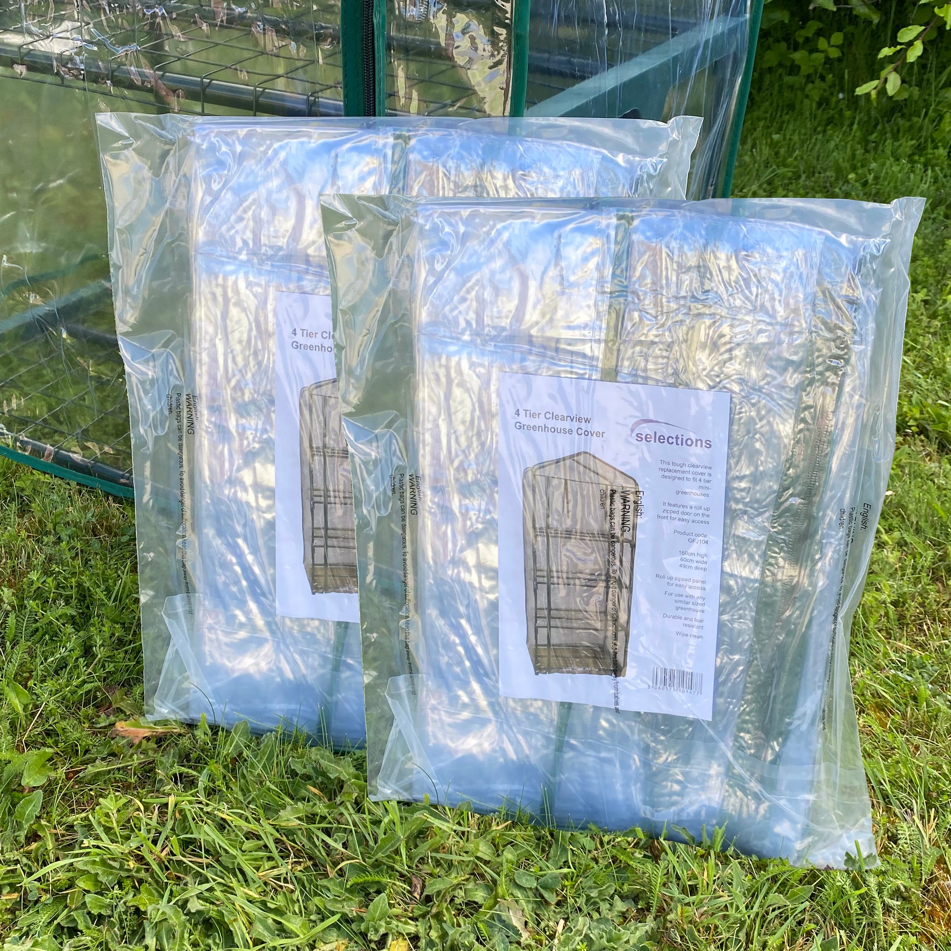 Two clear plastic replacement covers for a 4 Tier Mini Greenhouse, packaged and placed on grass.