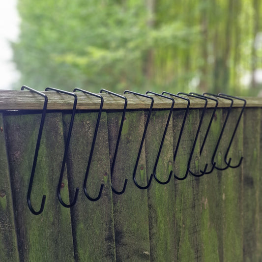 A series of black metal hooks attached to a wooden fence, designed to hold items for hanging.