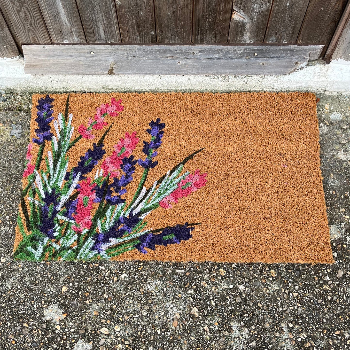 A coir doormat with a wildflower print placed on a concrete surface.