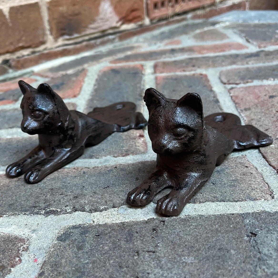 Two brown cast iron cat-shaped door wedges on a brick floor.