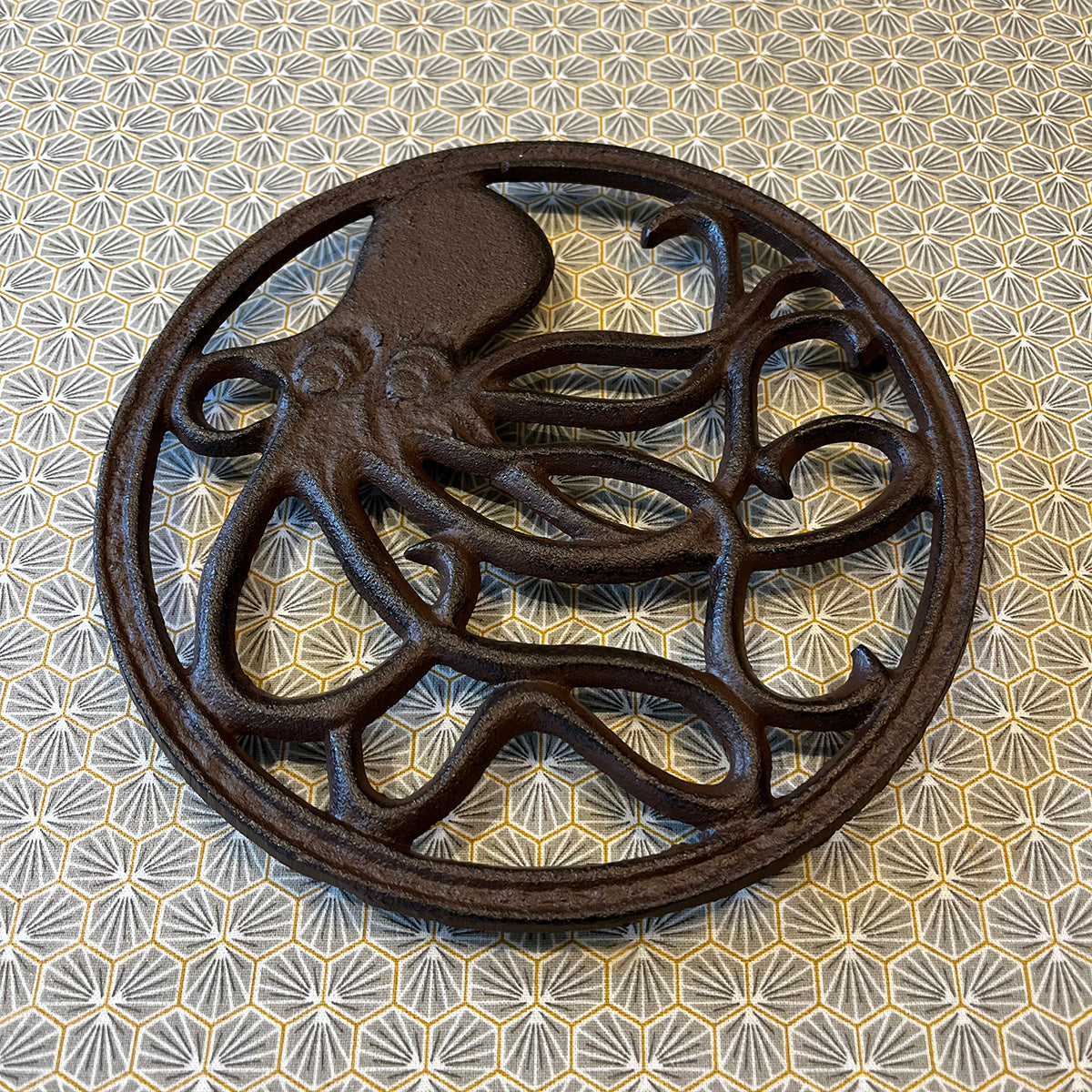 A round cast iron trivet with a relief sculpture of an octopus in the center, with a patterned background.