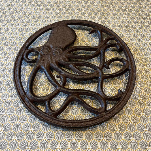 A round cast iron trivet with a relief sculpture of an octopus in the center, with a patterned background.