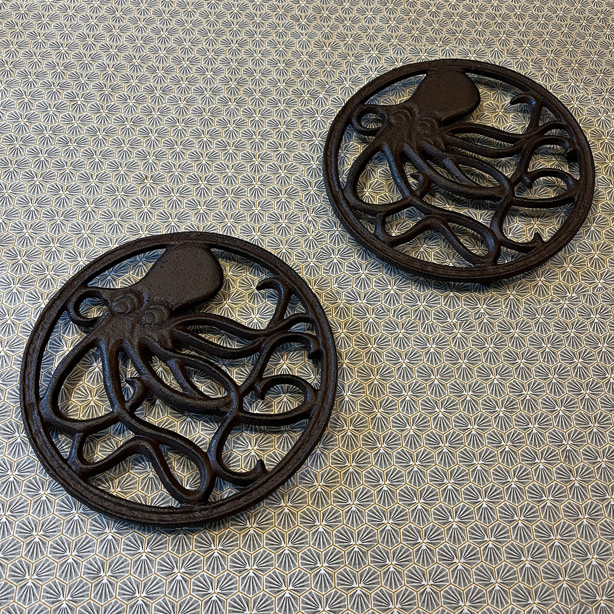 Two round black cast iron trivets with an octopus pattern in the center, placed on a table with a blue and white floral pattern.