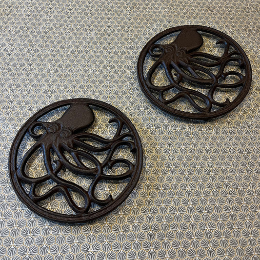 Two round black cast iron trivets with an octopus pattern in the center, placed on a table with a blue and white floral pattern.