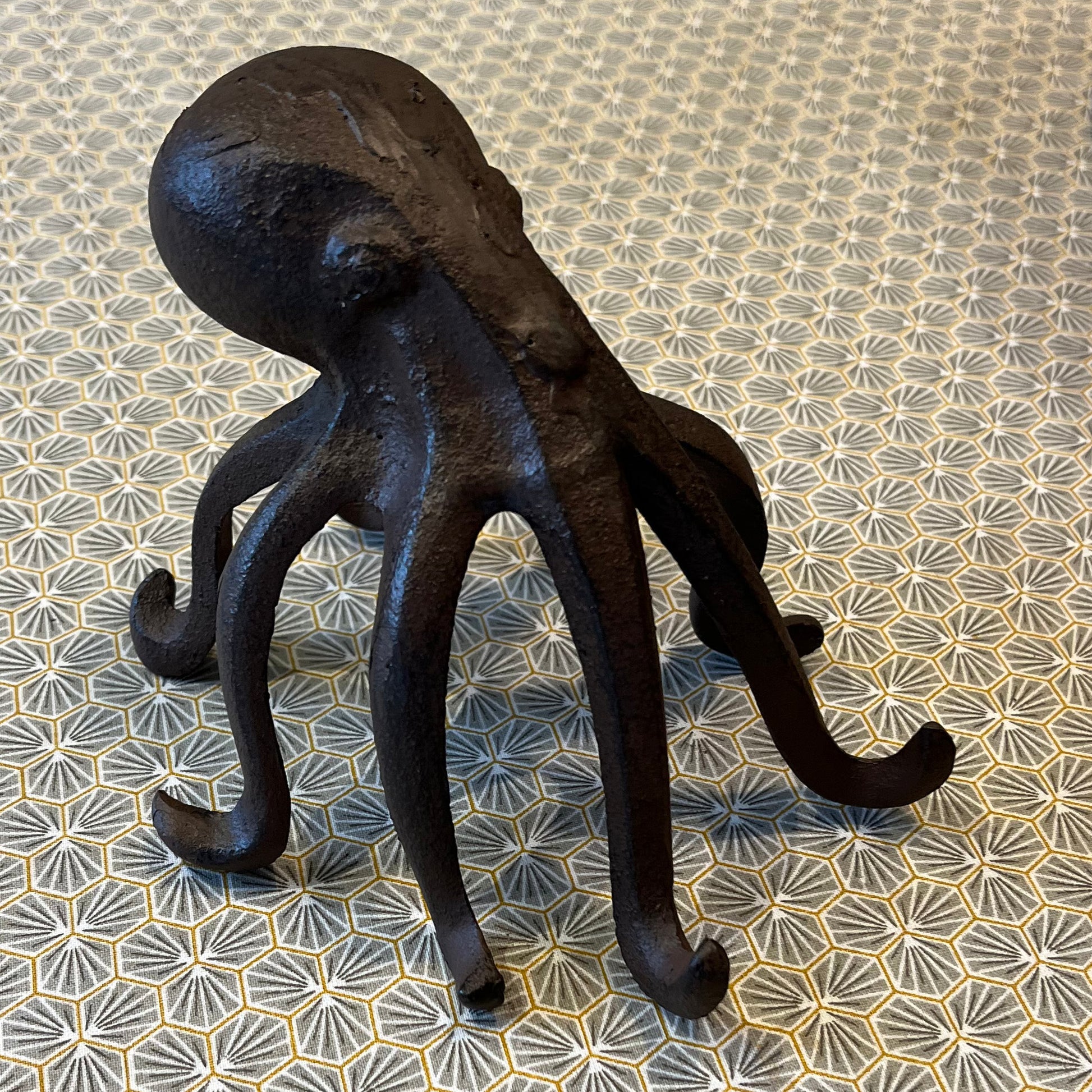 A black cast iron octopus-shaped phone holder with outstretched tentacles, standing on a patterned surface.