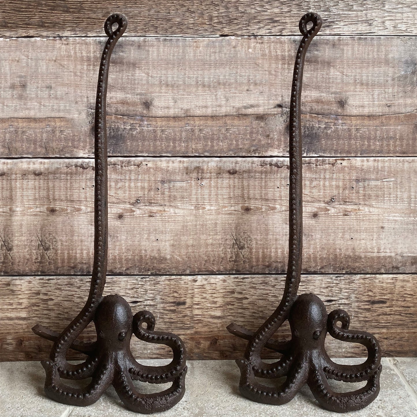 Two cast iron octopus-shaped toilet paper holders with rolls placed on their tentacles, set against a wooden backdrop.