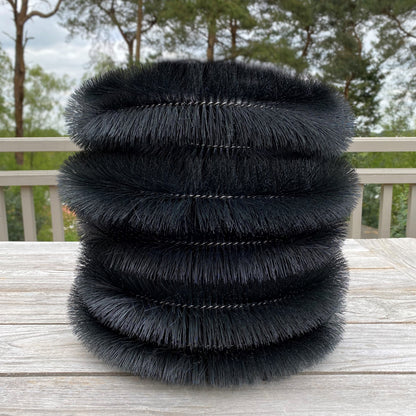Stack of black feathered cylindrical objects gutter protection brush on a wooden surface with a blurred natural background