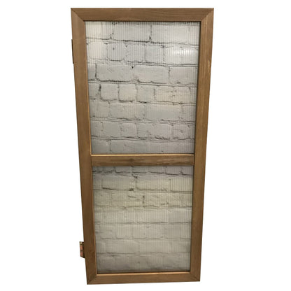 A wooden framed door panel with a mesh insert, presumably for ventilation, against a white brick background.