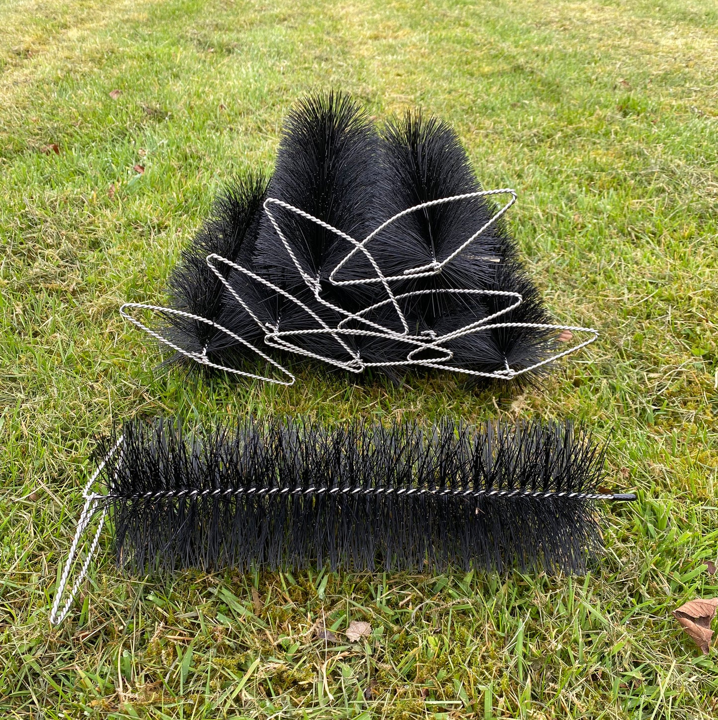 Two black gutter brusg plugs with bristle heads on a grassy background