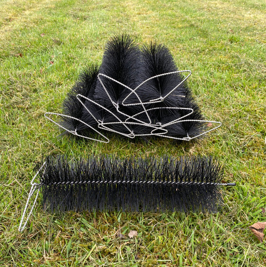 Two black gutter brusg plugs with bristle heads on a grassy background